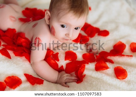 A brown-eyed little girl in kisses from a lipstick lies on the bed. Child in red rose petals.