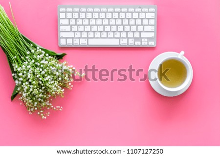 Cosy spring work desk concept. Computer keyboard, cup of tea and bouquet of lily of the valley flowers on pastel pink background top view copy space