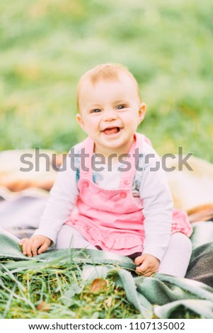 Portrait of happy joyful child in pink dress over green grass background. Happy little baby girl in the park. Family concept