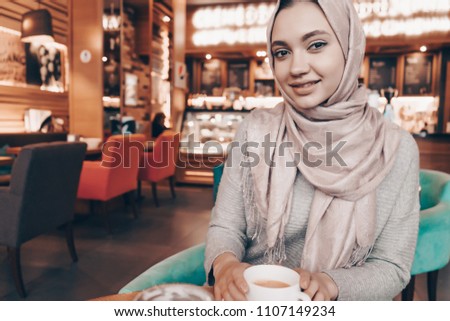 beautiful Arab girl in hijab sits in a cozy restaurant and drinks fragrant coffee