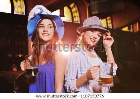 two cute young girlfriends in Bavarian hats smiling at the bar background during the celebration of the Oktoberfest