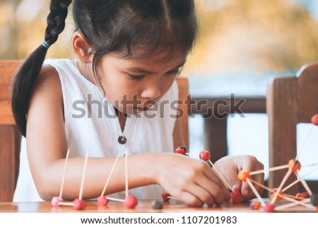 Cute asian child girl playing and creating with play dough and toothpick. Child concentrated with play dough building a molecule model.