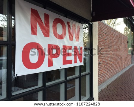 the new store hangging the red font on the white vinyl now open sign  the on the windows of store near the side walk