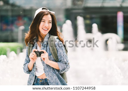 Young beautiful Asian backpack traveler woman using digital compact camera and smile, looking at copy space. Journey trip lifestyle, world travel explorer or Asia summer tourism concept