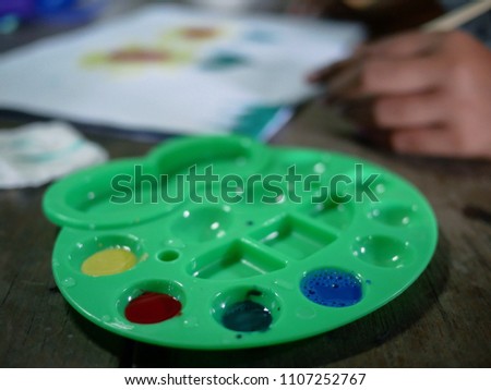 watercolor palette with blurred of hand kid painting color on the paper.