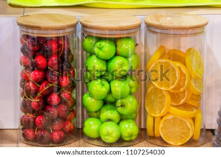 Advertising, Business, Food Concept - Interior design with colorful decorative glass bottles. Fake fruit, Green apple, Cherry, Lemon in glass jars. Food model for shop presentation. Select focus   