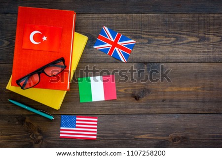 Language study concept. Textbooks or dictionaries of foreign language near flags on dark wooden backgrond top view copy space