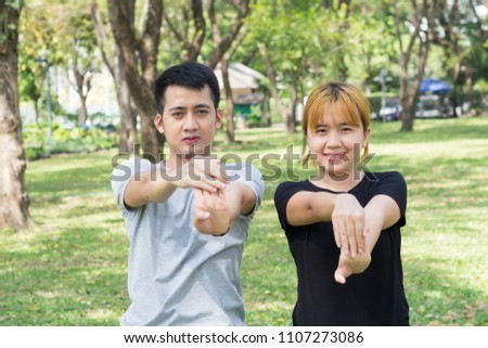 Asian sweet couple warm up their bodies by stretching arms before morning jogging exercise in the park surrounded with nature and warm light sunshine. lover couple exercise together outdoor with love.