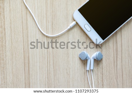White earphones with smartphone on office wooden desk background