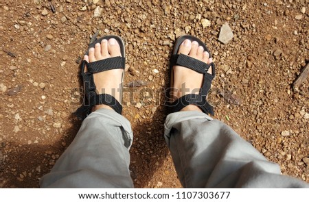 The foot wears black sandals on the floor.