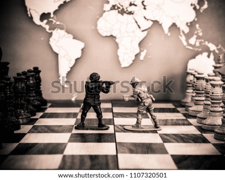 Various chess pieces and plastic soldiers are on the chessboard. In the background is a map of the world.