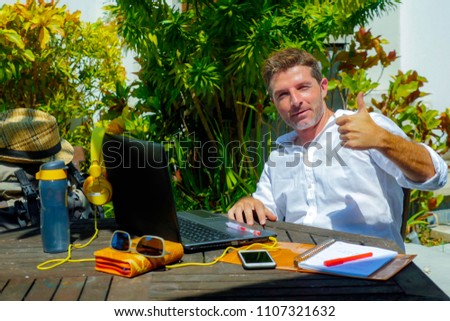 young attractive and happy digital nomad man working outdoors from coffee shop with laptop computer giving thumb up relaxed and confident in traveler and business travel lifestyle concept