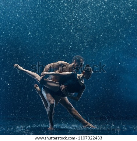 The couple of ballet dancers dancing under water drops and spray. Young caucasian and afro american models. Man and woman dancing together. Ballet and contemporary choreography concept. Art photo