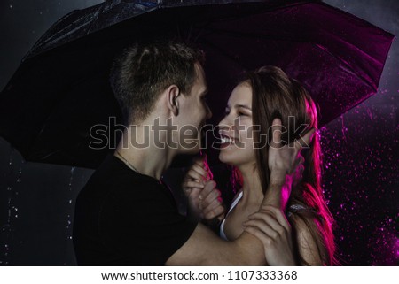 Couple young Teens stand together with black umbrella and colored light behing