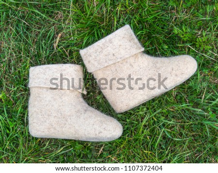 Cold summer. White felt boots on green grass background