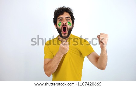 Sport fan screaming for the triumph of his team. Man with the flag of Brazil makeup on his face and yellow t-shirt.