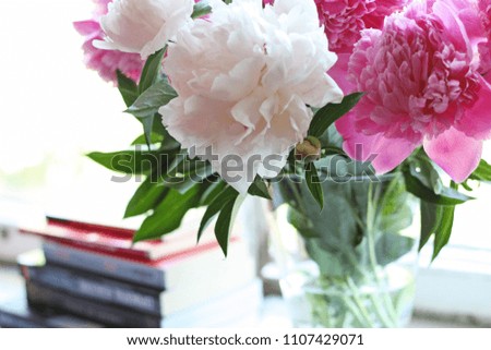 Still life with beautiful pink and white peony in transparent glass vase and books
