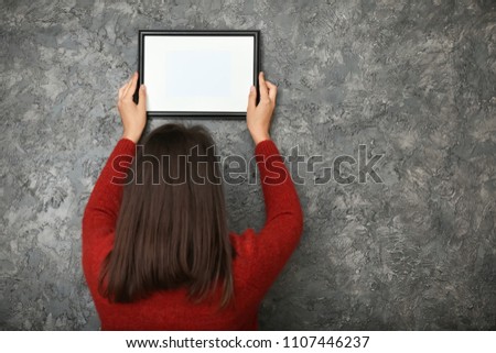 Woman hanging picture frame on dark textured wall