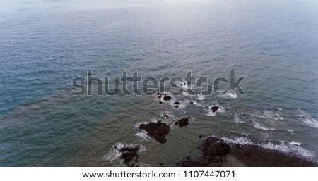 Amazing rocky beach shore. Picture of brown and black rocks surrounded by blue water.