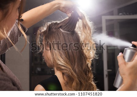 Back view of professional hairdresser fixing a coiffure with curls of a young client using a hair spray in a beauty salon Royalty-Free Stock Photo #1107451820