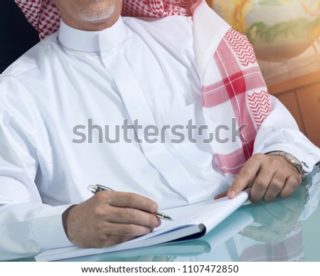 Smiling Senior Saudi Businessman Hand Writing At His Desk