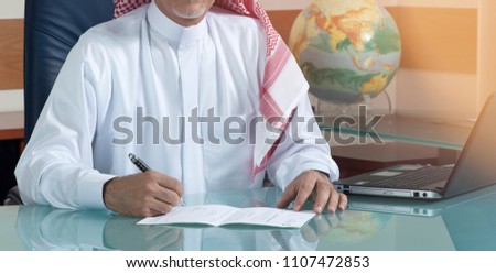 Senior Saudi Businessman Hand Writing At His Desk with Laptop Royalty-Free Stock Photo #1107472853