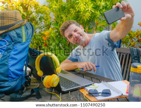young attractive and happy digital nomad man working outdoors with laptop computer cheerful taking selfie pic with mobile phone in freelancer and independent job success concept