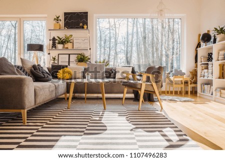 Low angle of warm bright living room interior with armchair at wooden table next to corner sofa
