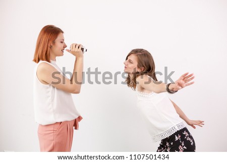 Two female friends playing with an action camera in studio over a white wall