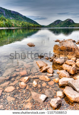 idyllic mountain lake with woodland reflections and red rocks in the foreground