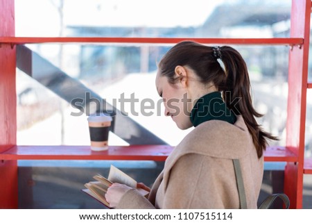 Young girl reading a book near the shelves with coffee and books, social library, a place of exchange of books.