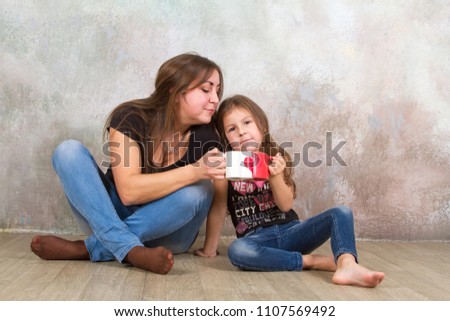 Cute little girl and her beautiful young mother sitting together on the floor.