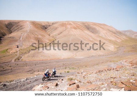 Motorcyclists driving through a stony track of some desert mountains living their travel adventure