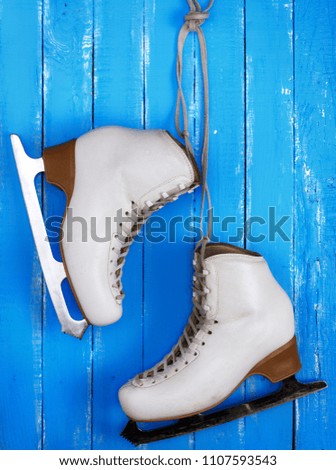 pair of white leather female skates for figure skating hanging on a blue wooden background