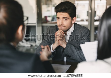 Business, career and placement concept - nervous uptight man 30s worrying and putting fists together during job interview in office with collective of specialists Royalty-Free Stock Photo #1107596555
