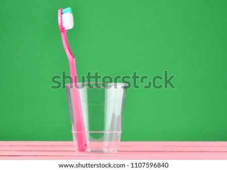 Pink toothbrush in a transparent cup on a green pastel background, minimalist trend
