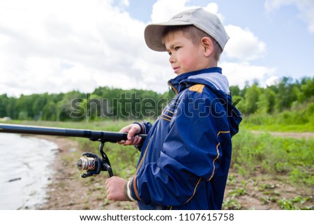 the boy on the river bank with a fishing rod is fishing