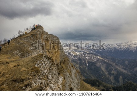 Photo of tourist walking through the edge of a mountain and in the background a big Mountains in fog and clouds