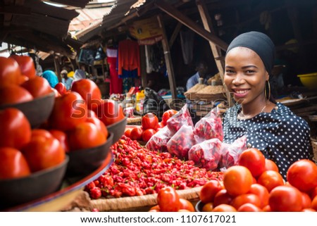 a girl in a typical african local market, at a stand where they sell tomatoes and pepper Royalty-Free Stock Photo #1107617021
