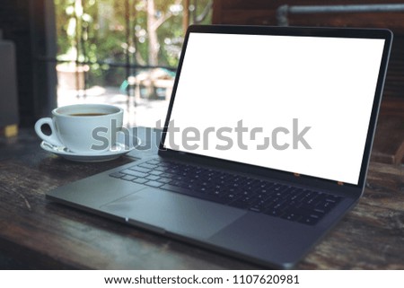 Mockup image of laptop with blank white desktop screen and coffee cup on wooden table in modern cafe