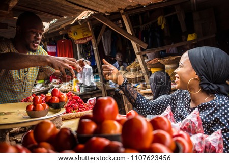 a guy selling tomatoes to a girl in a typical local african market Royalty-Free Stock Photo #1107623456