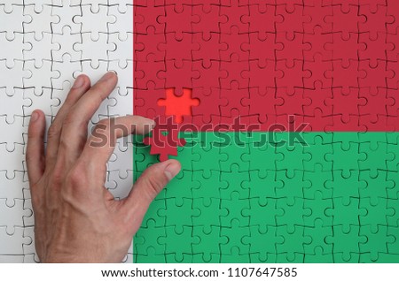 Madagascar flag  is depicted on a puzzle, which the man's hand completes to fold