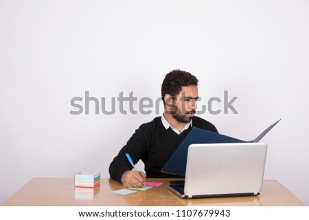 Handsome businessman wearing a formal outfit, sitting in his office reading a file and writing notes