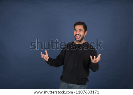 Handsome young man wearing casual outfit standing and opening his hand, looking so surprised and screaming, standing on a navy background