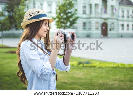 Pretty girl wearing hat taking picture with an old retro camera in the town in Europe