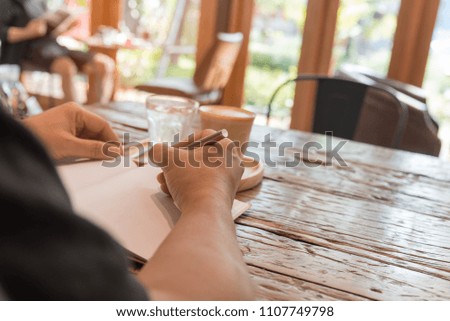 Close up picture of manâ€™s hands and a cup of cappuccino. Man is writing in his notebook with a pen in coffee cafe,copy space.