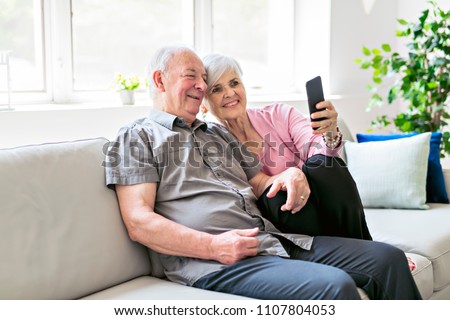 Affectionate attractive elderly couple sitting together on a couch taking selfie