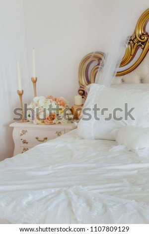 Fragment of bed and bedside table with flowers and candles. Elegant bedroom interior.