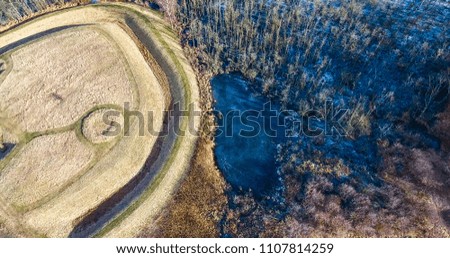 Rounded fields and frozen lake in winter scenario shot from air