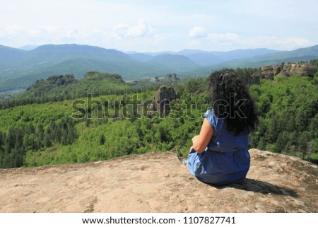 A young curly woman sitting on a rock high in the mountains 